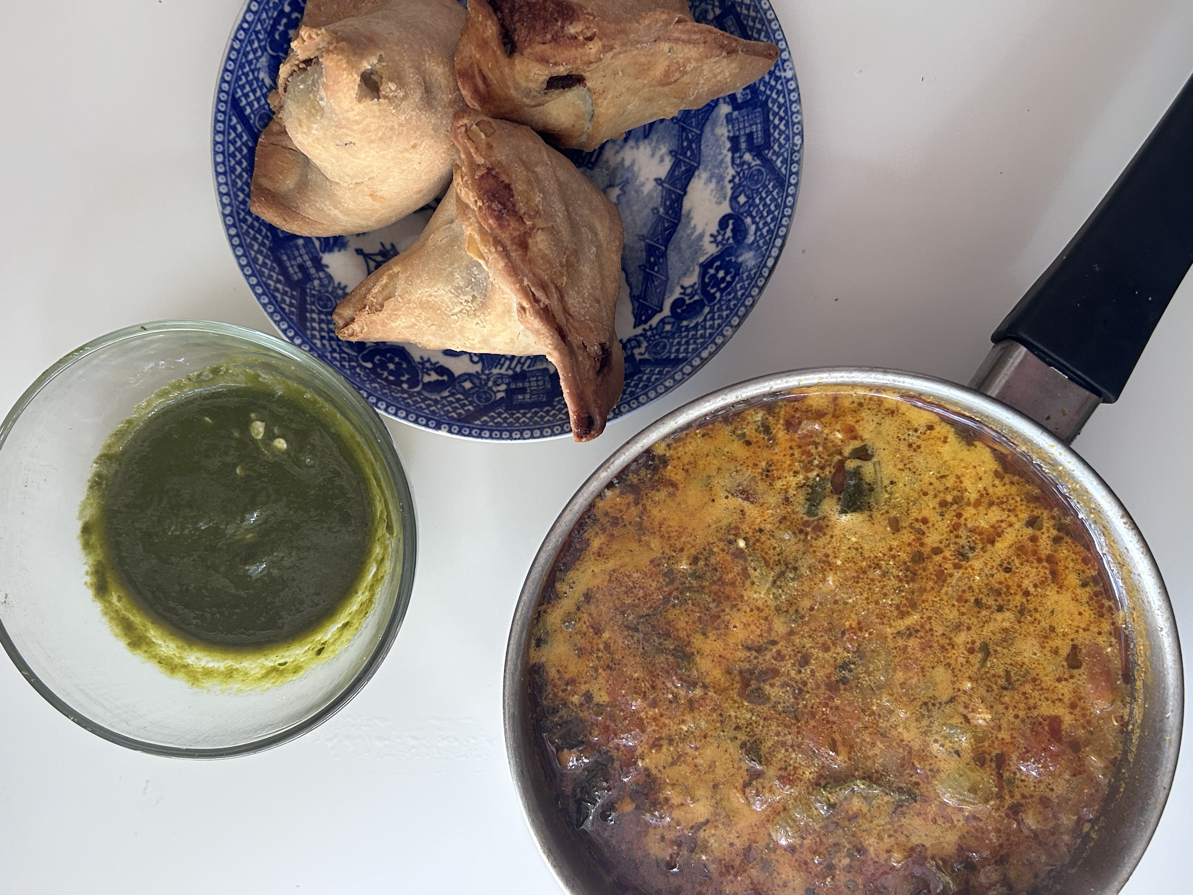 Samosas and green chutney beside a pan of simmering curry